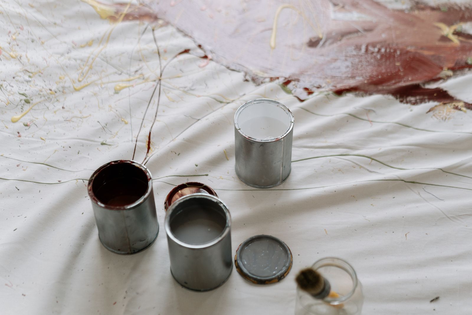 Three open paint cans on canvas with splattered paint, depicting an artistic setting.